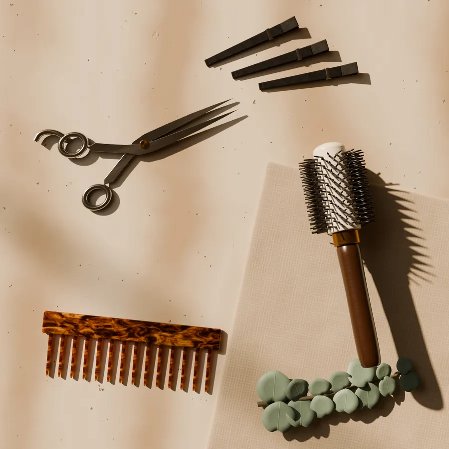 Shears, a wide-tooth comb, clips and a round brush laid out on pale stone and linen